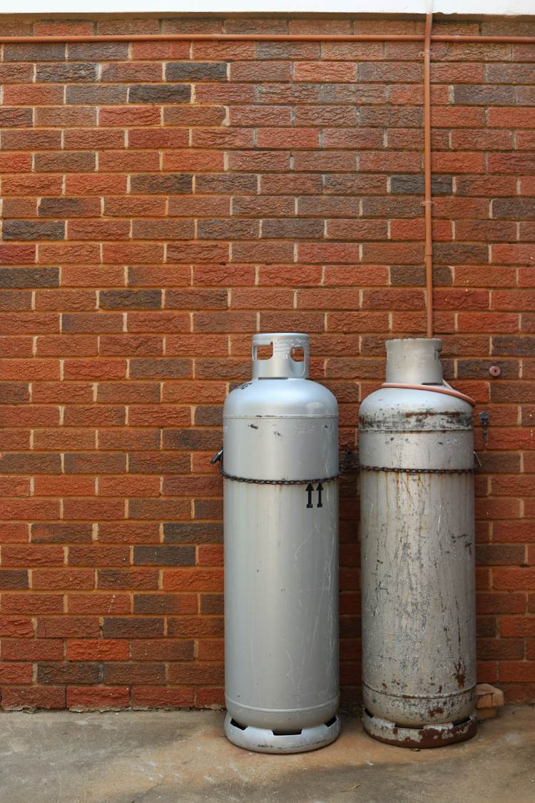 Two LPG gas cylinders standing against a brick wall