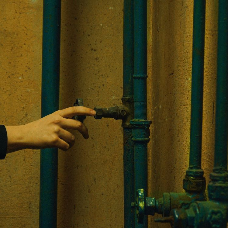 A hand reaching for a valve on the water pipes