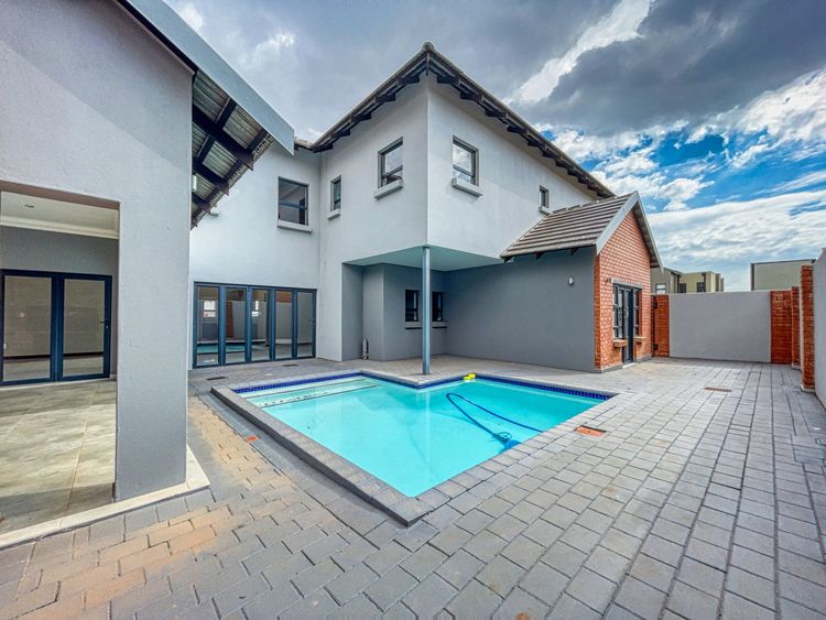 Swimming pool behind a house, with paving around it